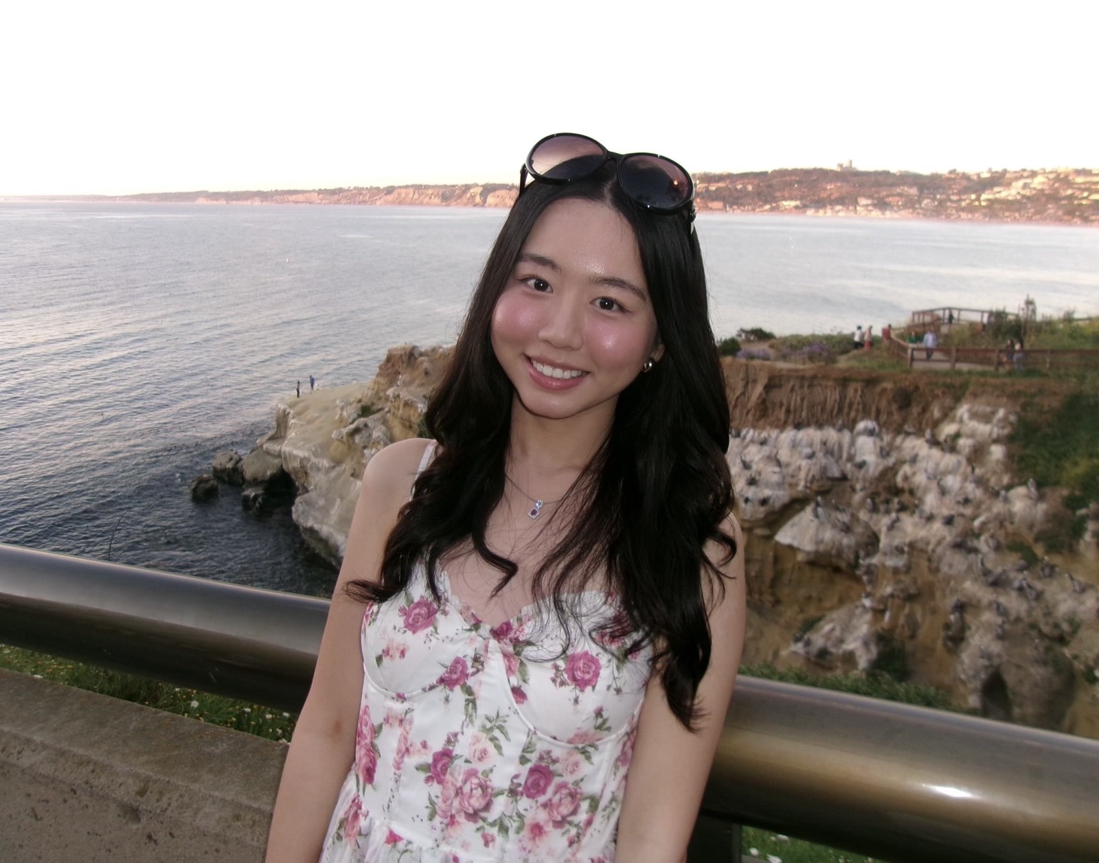 Joyce standing on the La Jolla Coast Walk Trail in San Diego, CA in a white floral dress and sunnglasses