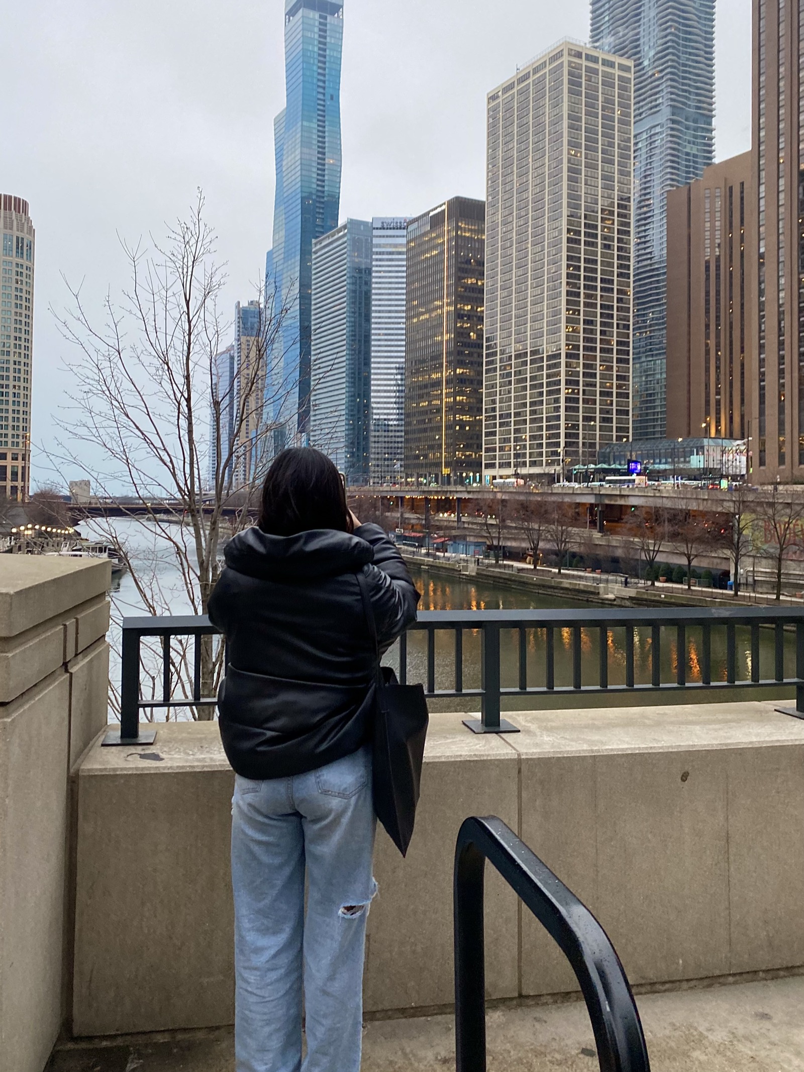 Joyce standing on the Chicago Riverwalk in a black puffer jacket and blue jeans