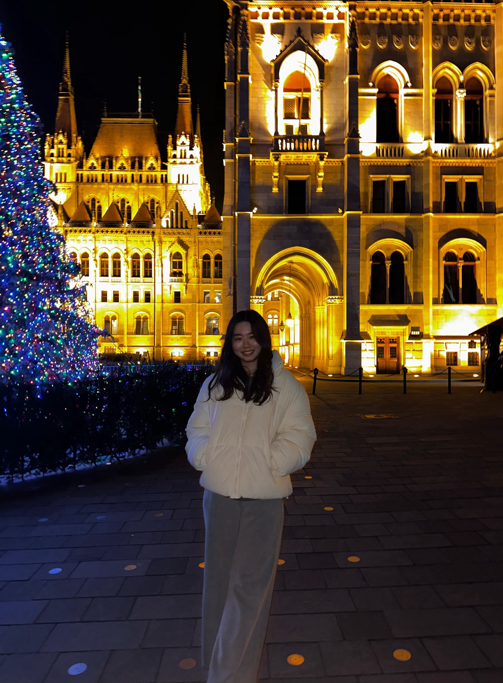 Joyce standing in front of the Hungarian Parliament in a white puffer jacket
