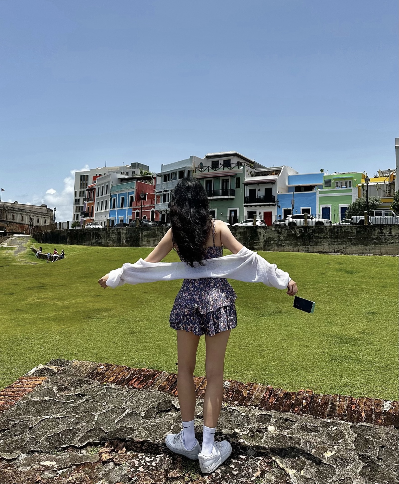 Joyce posing in front of the Castillo San Felipe del Morro in Old San Juan, Puerto Rico in a floral dress and white cardigan