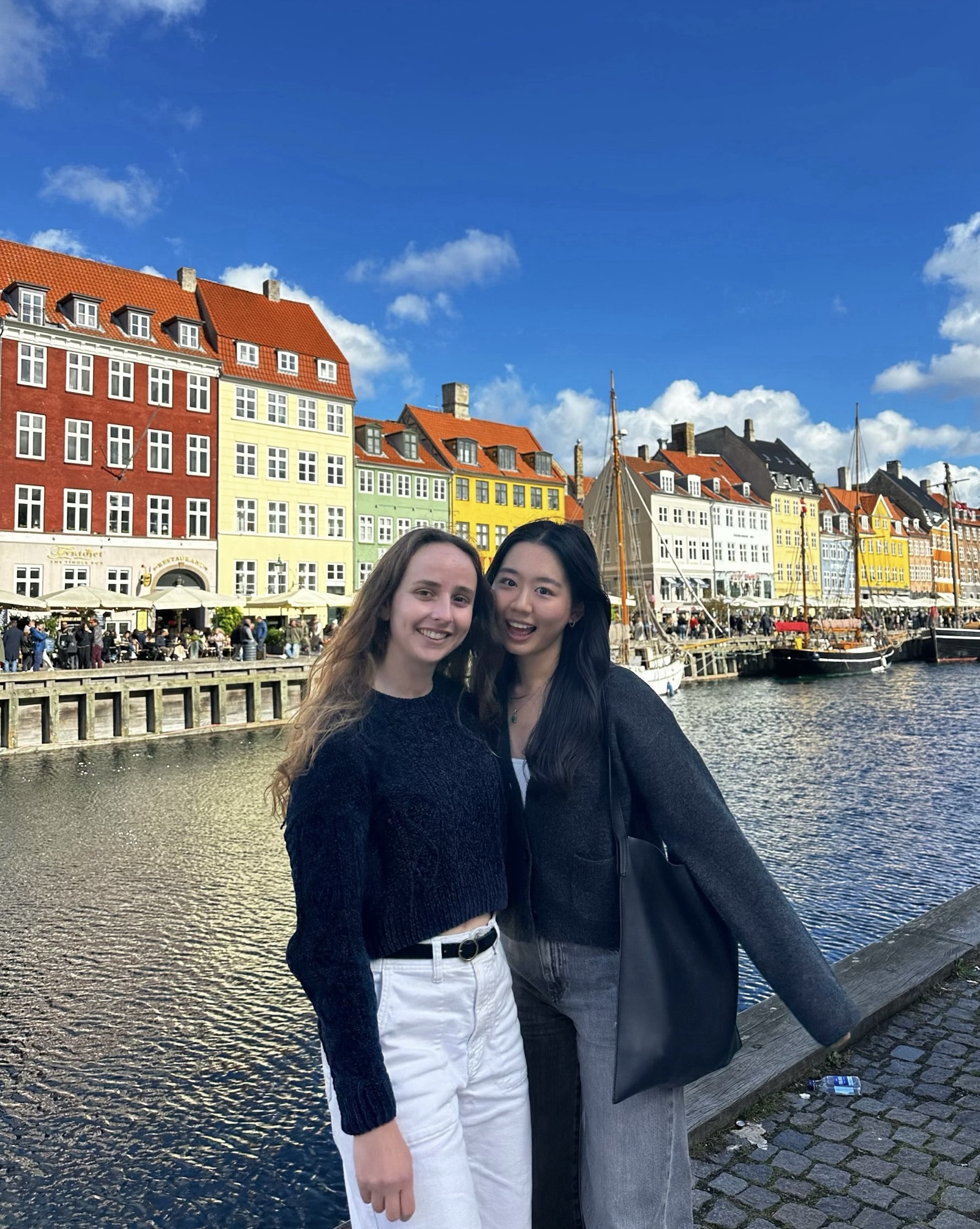 Joyce and her friend standing in front of the Nyhavn in Copenhagen in a dark grey cardigan and pants